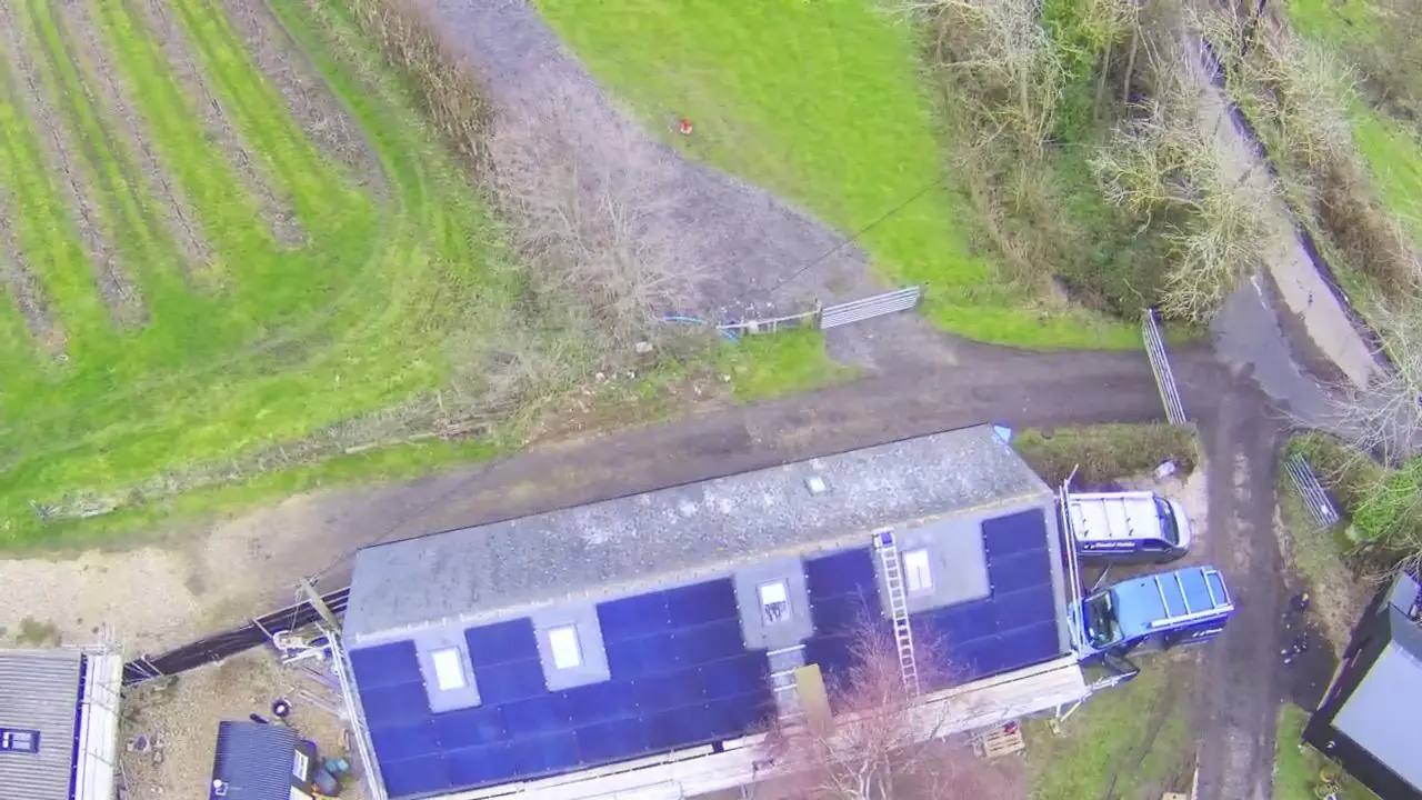 Aerial view of a long single storey building with solar panels covering the full roof slope, a van and a ladder in the yard alongside.