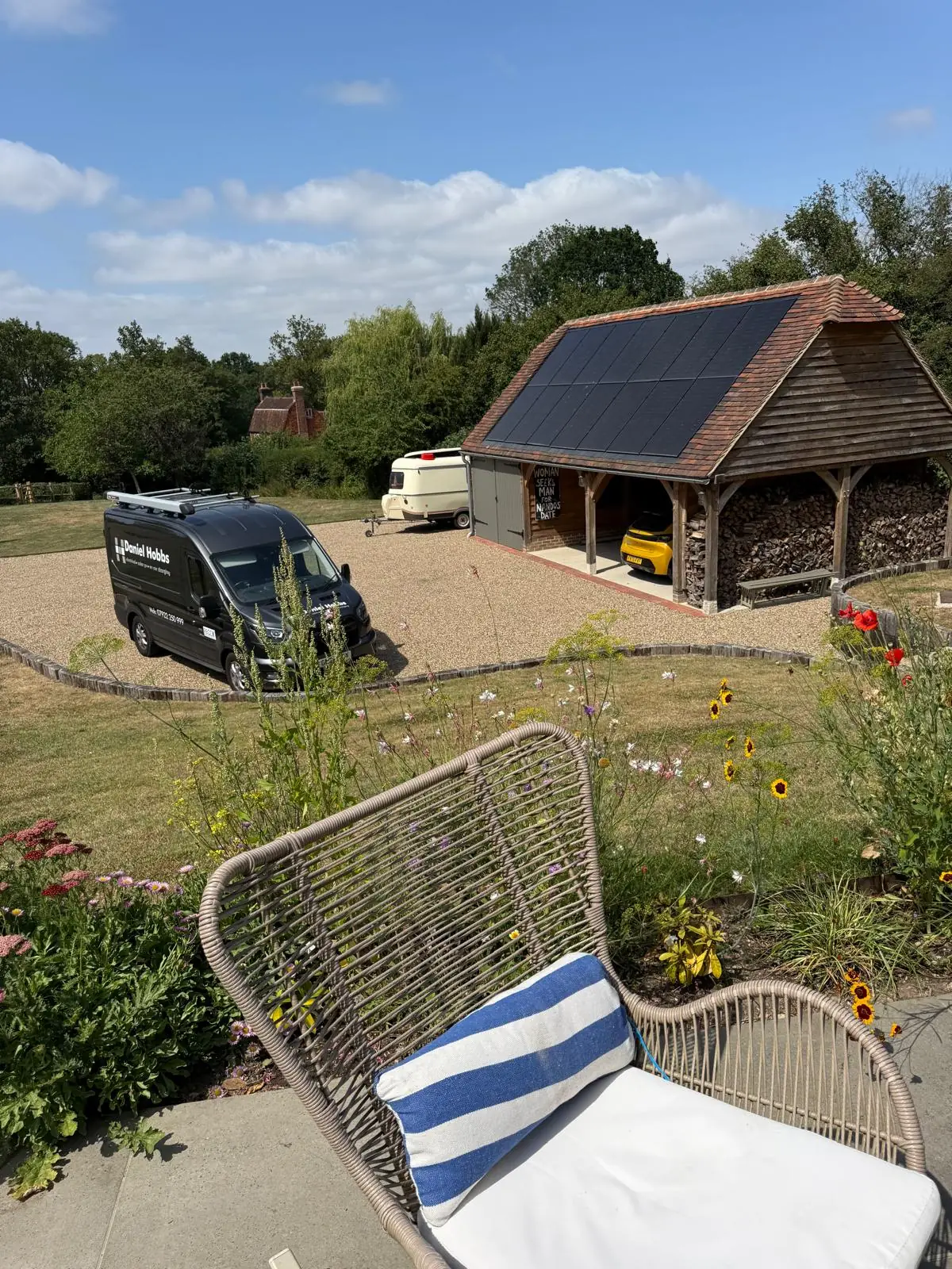 An oak framed cartlodge with a log store, a GSE in roof array set into its clay tile roof, and the company van on the gravel drive.