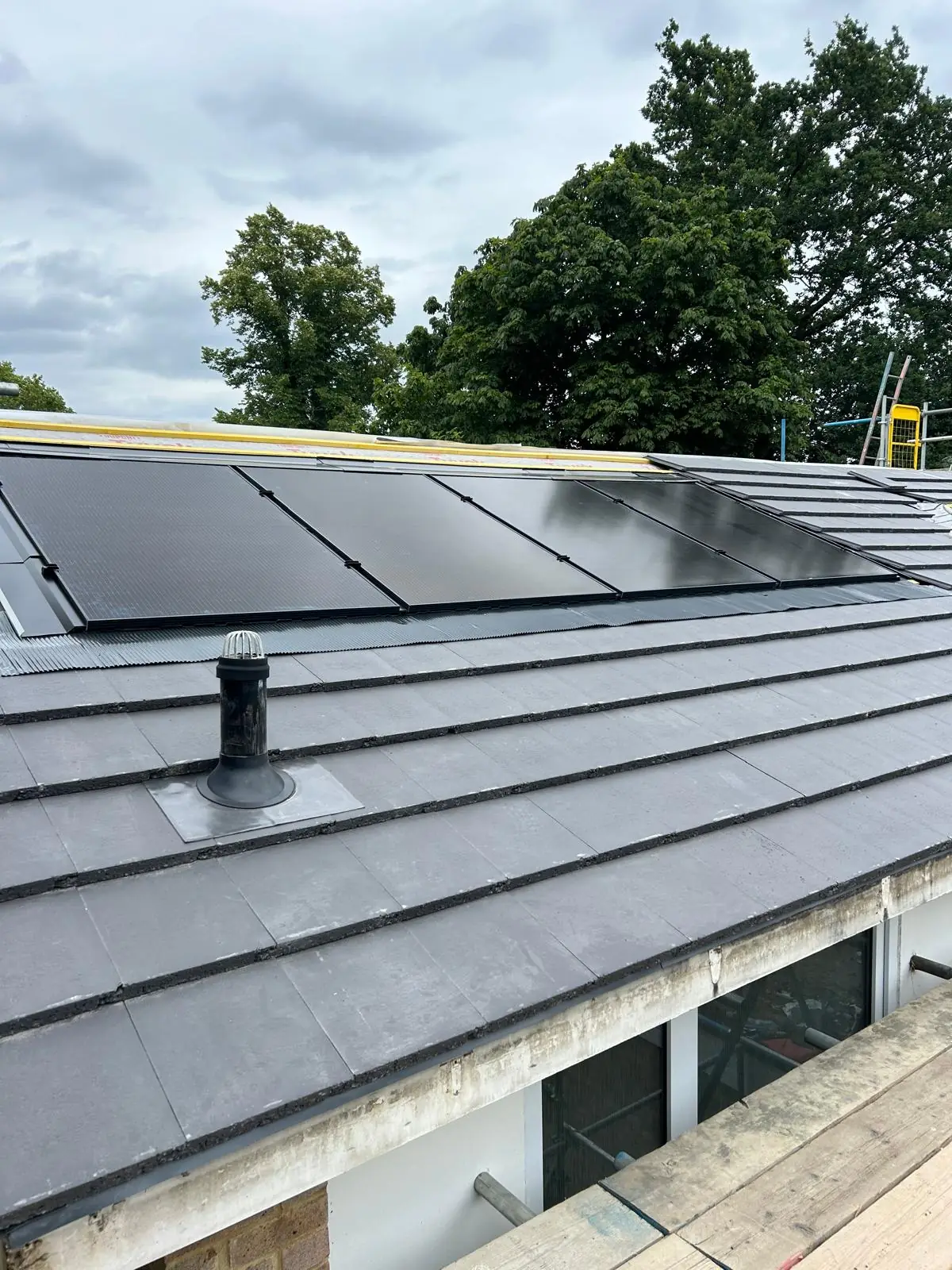 An in roof all black array set flush into a slate roof, seen against the sky.