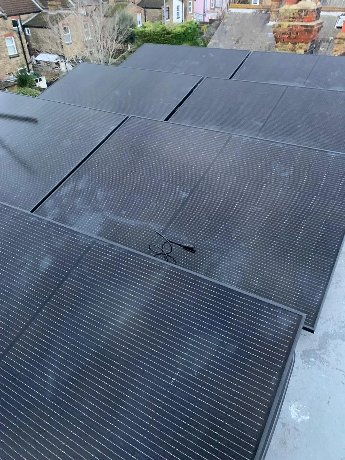 Looking down over a large all black solar array covering a roof, with terraced houses and gardens beyond.